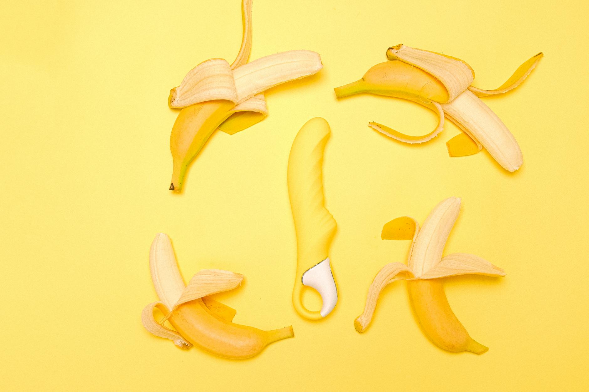 Creative flat lay of a yellow silicone vibrator surrounded by peeled lemons on a yellow background.