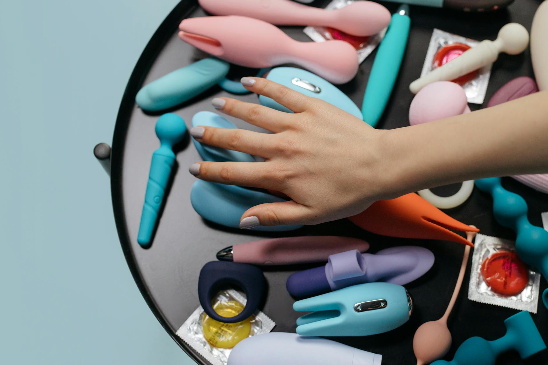 Two hands reaching together over a collection of colorful adult toys arranged on a table, symbolizing shared exploration and intimacy