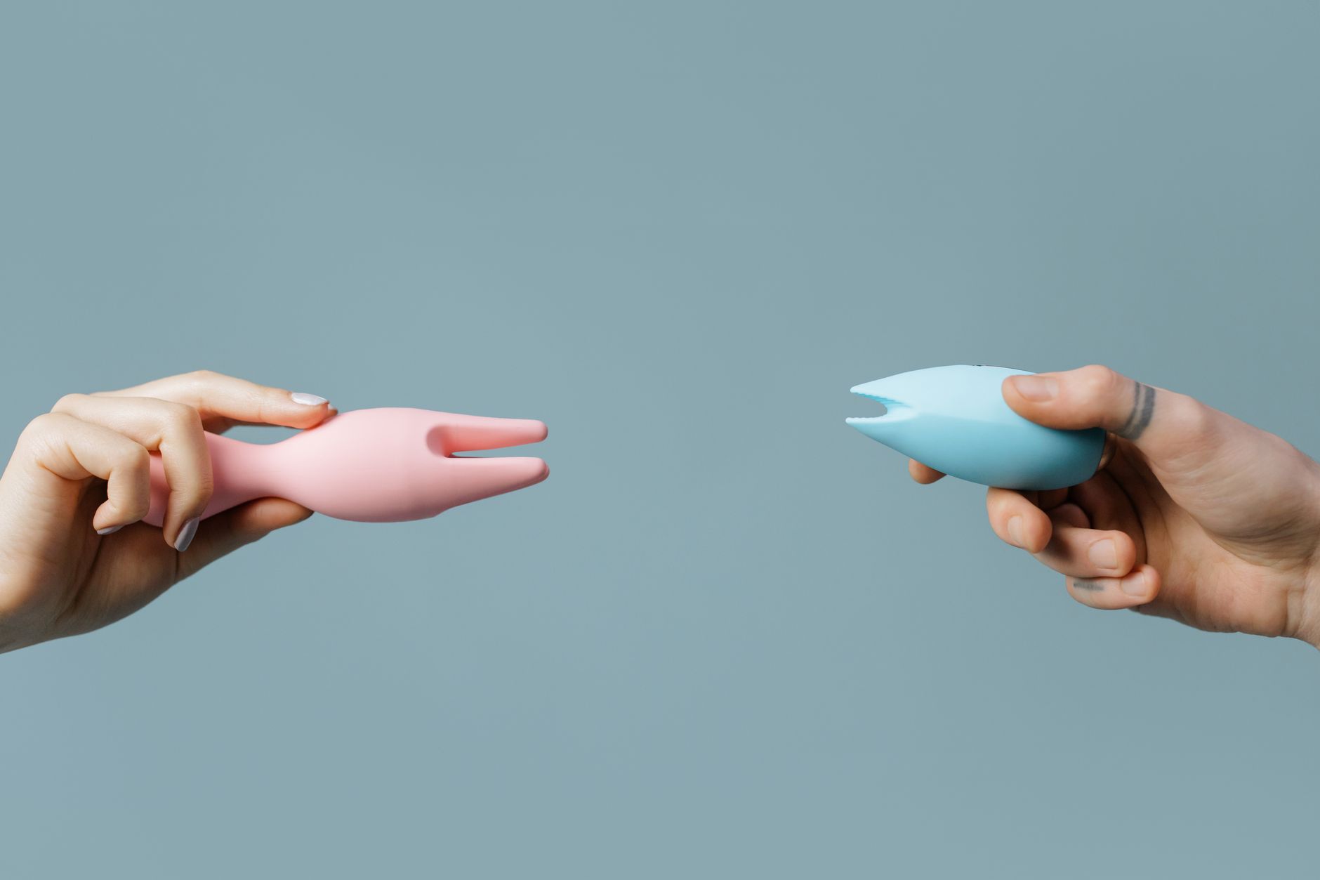 Woman holding blue and pink silicone vibrators in a contemplative manner