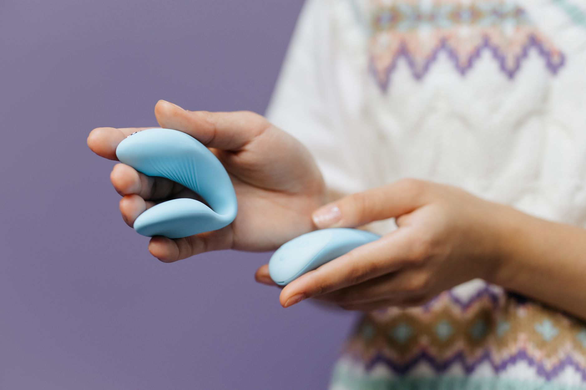 Hands holding a sleek blue Lemon clitoral vibrator against a purple background.