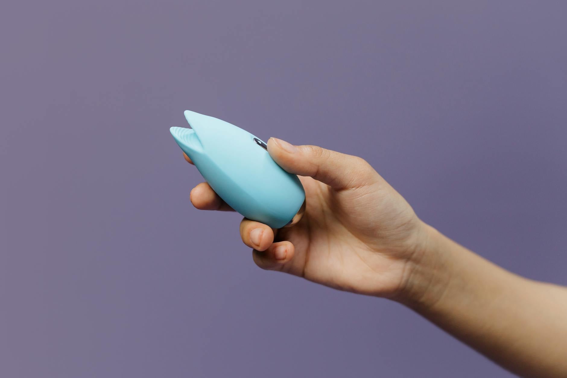 A blue silicone sex toy held in hand against a purple background, promoting self-love and body appreciation